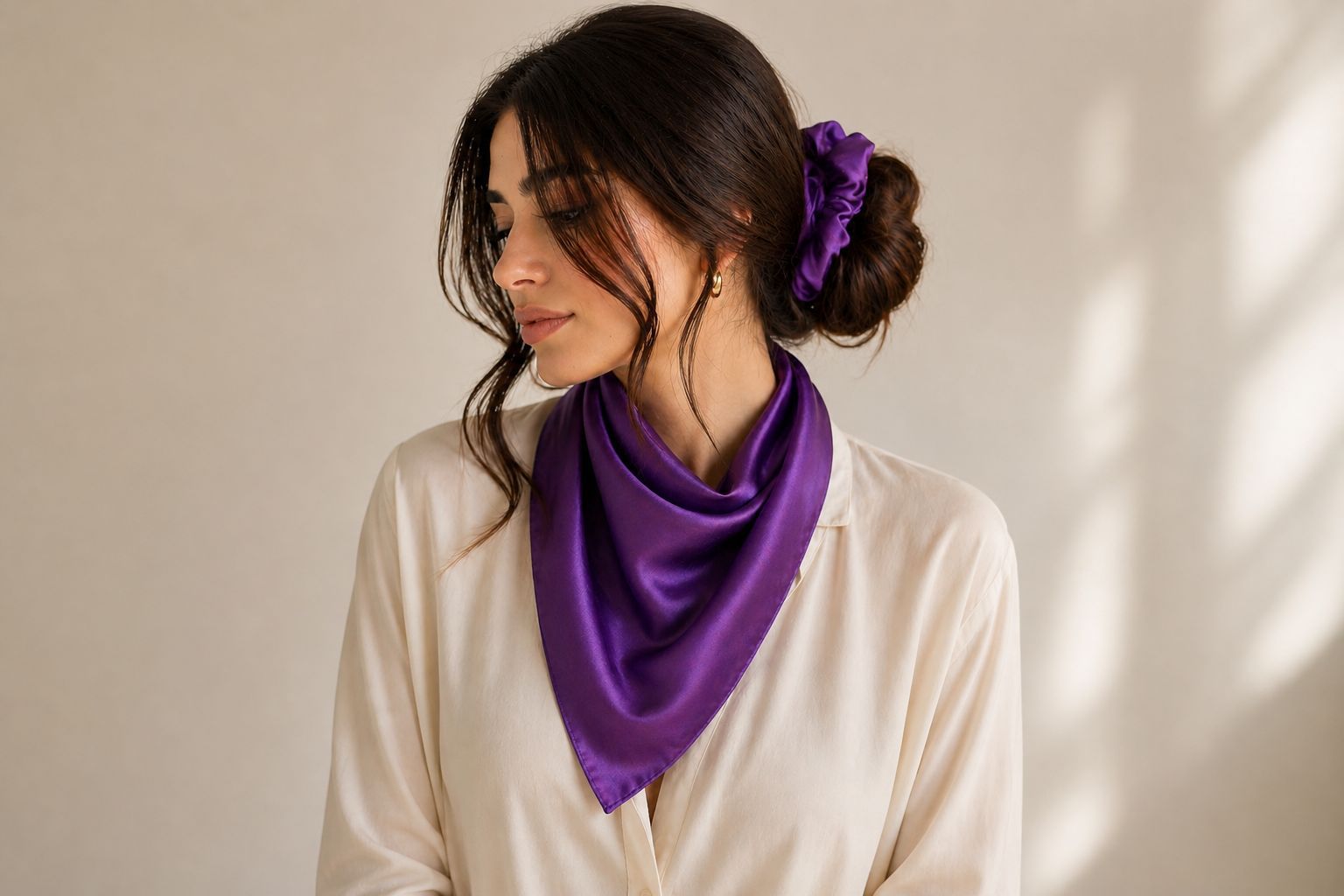 Woman wearing a purple scarf and hair accessory against a neutral background