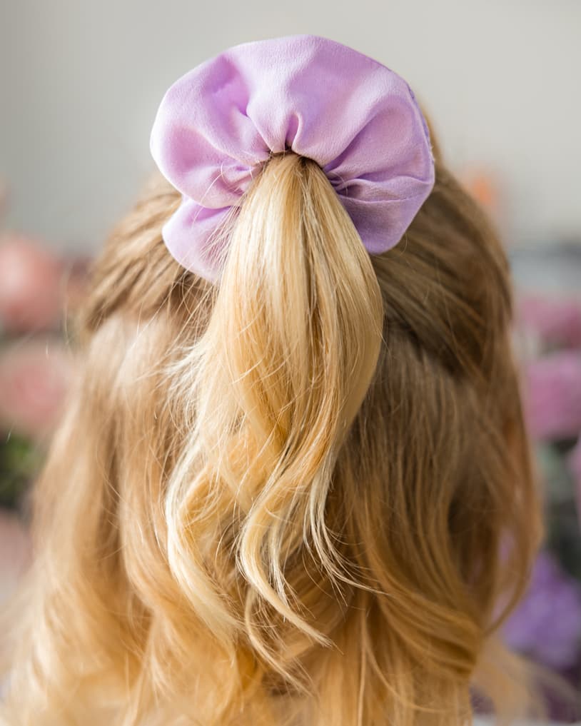 Purple scrunchie on a person's hair with a blurred background